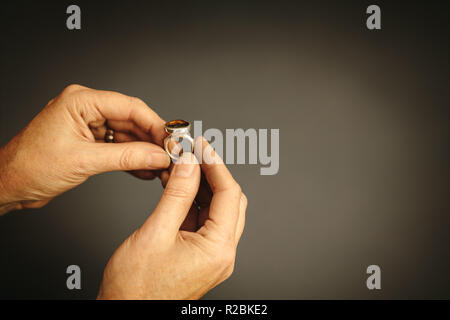 Close up of woman goldsmith hands looking and inspecting a ring with gem stone. Jewelry designer examining a ring against grey background with copy sp Stock Photo