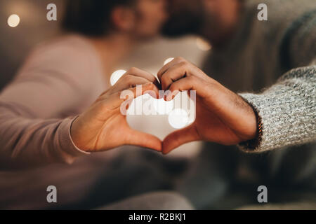 Romantic couple making the symbol of heart with their hands. Man and woman kissing each other while making the love sign with their hands. Stock Photo