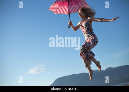 Young woman jumping holding pink umbrella Stock Photo