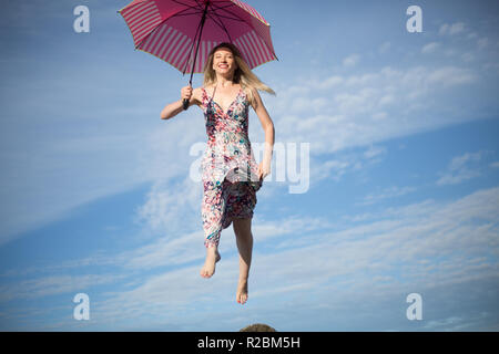 Young attractive happy female jumping in sky with umbrella Stock Photo
