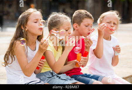 cheerful boy and girls in elementary school age blowing bubbles outdoors. Selective focus Stock Photo