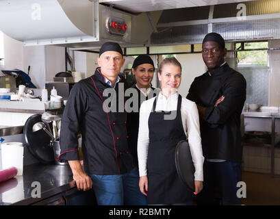 Successful multinational team of restaurant staff standing together in professional kitchen Stock Photo
