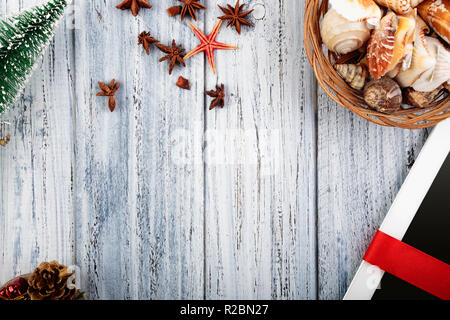 Presents wrapped with red ribbon and new year's attributes, Christmas star, bumps, basket with sea shells on vintage wooden background with space for  Stock Photo