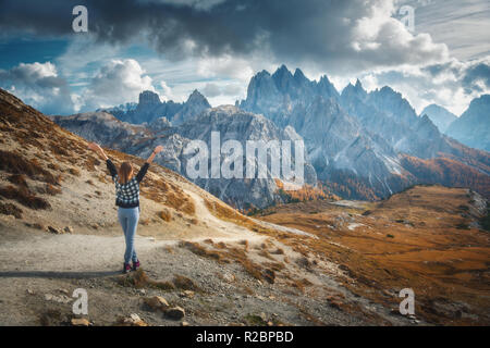 Young woman with raised up arms and majestic mountains at sunset in autumn in Dolomites, Italy. Landscape with happy girl, dramatic sky with clouds, o Stock Photo