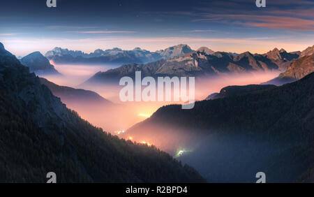 Mountains in fog at beautiful night in autumn in Dolomites, Italy. Landscape with alpine mountain valley, low clouds, forest, purple sky with stars, c Stock Photo