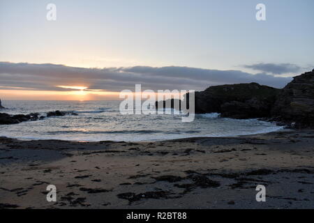 View of a small cove, by Trearddur Bay on the beautiful Welsh island of Anglesey at sunset. Waves break gently on the sands as the sun goes down. Stock Photo