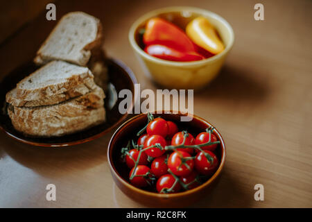 still life of bowl of fresh pepper, bowl of cherry tomatoes and a plate of sliced bread Stock Photo
