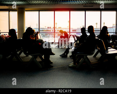 BANGKOK, THAILAND - November 1, 2018 : Passenger sitting on waiting chairs near the window glass waiting for boarding to the aircraft on sunset in eve