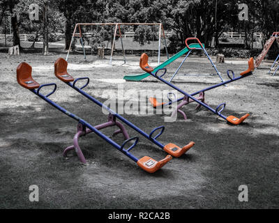 Empty seesaw, chain swing and playground slide in old playground in public park. Childhood memories concept. Stock Photo