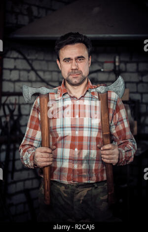 Portrait of blacksmith with new axes at forge. Looking through the camera Stock Photo