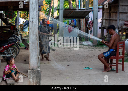 Don Det, Laos - April 24, 2018: Local man repairing a fishing net in front of a wooden house in southern Laos surrounded by his family