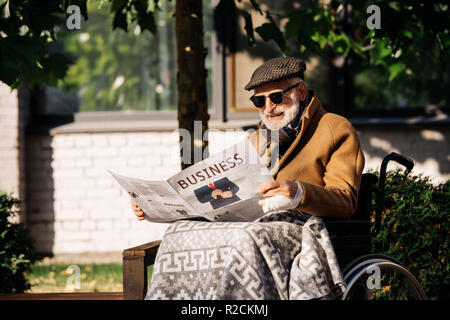 senior disabled man in wheelchair reading business newspaper on street Stock Photo