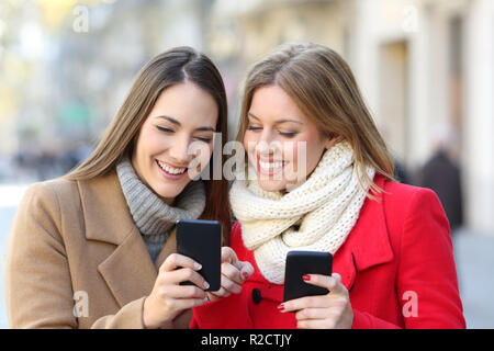 Friends consulting smart phone content in the street in winter Stock Photo