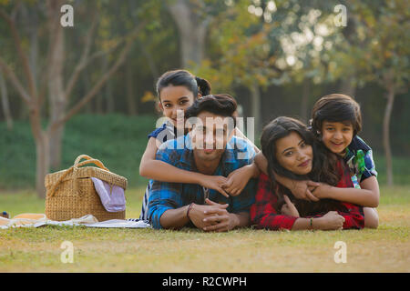 Happy man and woman on a picnic lying down in garden beside a picnic basket and their children lying on their backs. Stock Photo