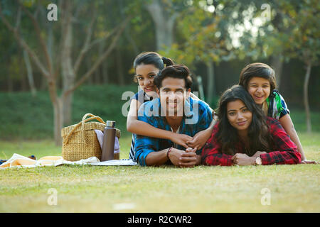 Happy man and woman on a picnic lying down in garden beside a picnic basket and their children lying on their backs. Stock Photo