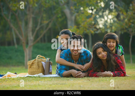 Happy man and woman on a picnic lying down in garden beside a picnic basket and their children lying on their backs. Stock Photo