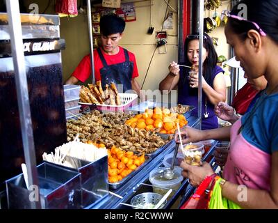 ANTIPOLO CITY, PHILIPPINES - NOVEMBER 13, 2018: Customers of a snack food kiosk pick their choice of fried food. Stock Photo