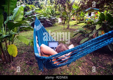 man lying in a hammock and working on a laptop at the garden Stock Photo
