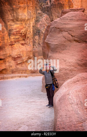 An Arabic man in a kaffiya takes a cell phone photo of the beautiful rock formations in Petra, Jordan Stock Photo