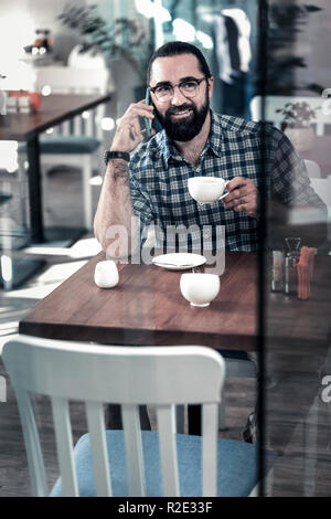 Pleasant mature man calling his wife waiting for her in cafeteria Stock Photo