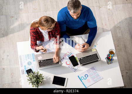 Serious colleagues using laptops while working with data Stock Photo
