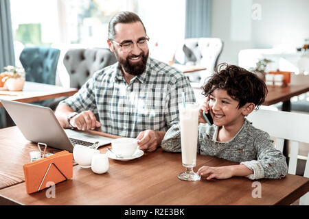 Beaming son speaking by phone with mother standing near father Stock Photo