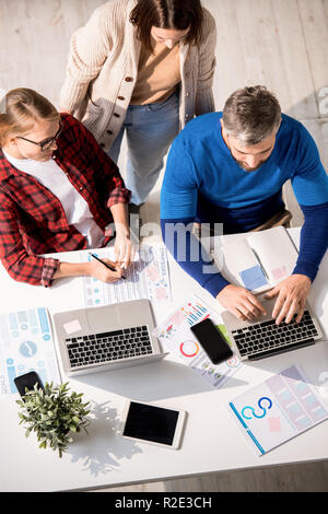 Serious thoughtful analysts busy with papers working on marketing project and analyzing data together in office Stock Photo