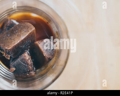 Close-up Coffee ice cubes in glass on wooden table top view. Frozen espresso cube. Stock Photo