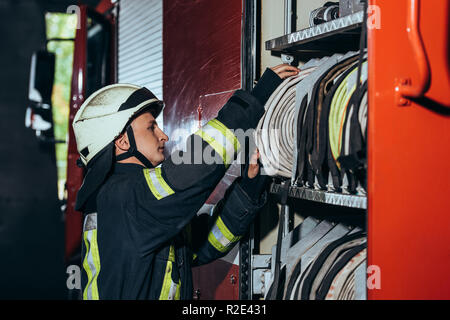 side view of fireman in protective uniform checking equipment in truck at fire station Stock Photo