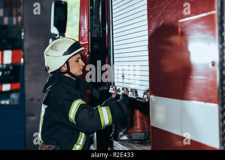 side view of fireman in uniform closing truck at fire department Stock Photo