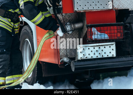 partial view of firefighter in protective uniform checking water hose Stock Photo