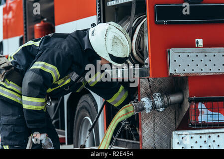 firefighter in protective uniform checking water hose in truck on street Stock Photo