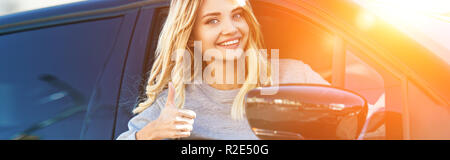 portrait of blond smiling woman showing thumb up while driving car Stock Photo