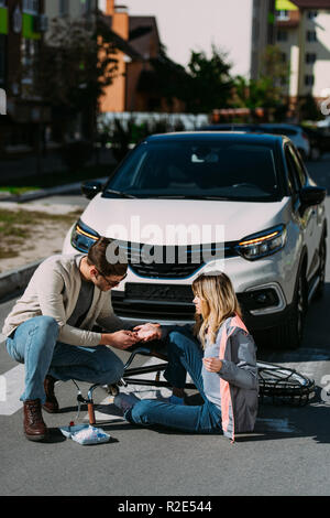 man getting first air to injured woman after car accident on road Stock Photo