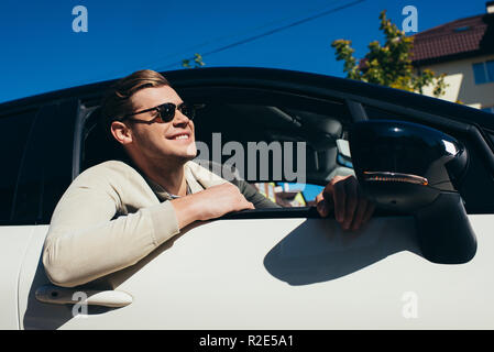 smiling young man leaning out car window of driving automobile Stock Photo