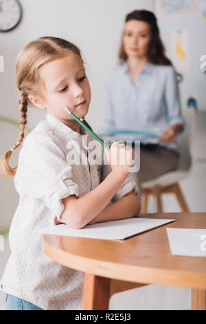 thoughtful little child drawing while psychologist with clipboard sitting blurred on background Stock Photo