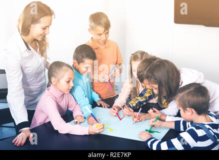 Professor and elementary age children drawing together one picture in ...
