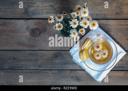 Cup of tea with chrysanthemum flowers and macaroons on the dark wooden surface, top view, copy space, cinematic color. Stock Photo