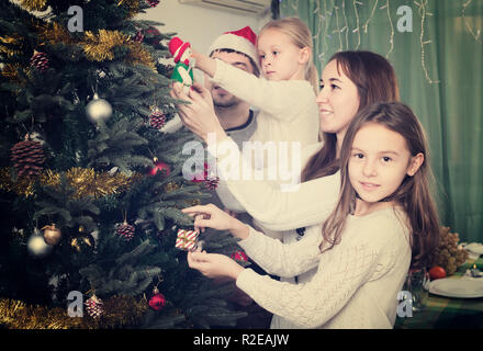 Happy parents with children decorating Christmas tree in big room Stock Photo