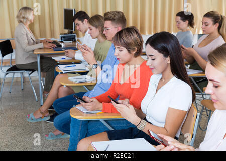 Students using smartphones to find necessary information on lecture in university class Stock Photo