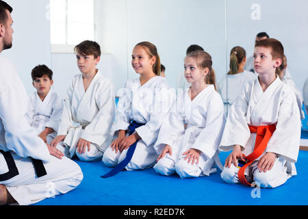 Young smiling man training new karate moves with kids during class. Focus on boy Stock Photo