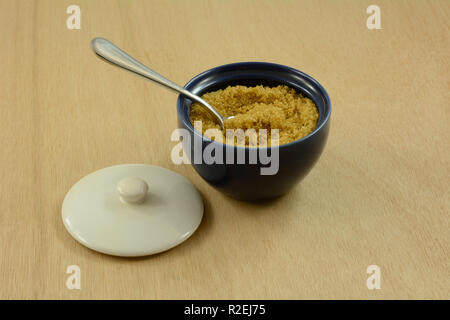 Brown sugar in blue sugar bowl with spoon inside and white lid on wooden table Stock Photo