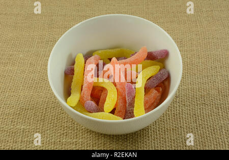 Yellow, orange and purple sour gummy worms candy in white bowl on burlap Stock Photo