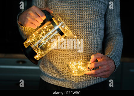 Crop man in knitted sweater with garland in cup and coffee press Stock Photo