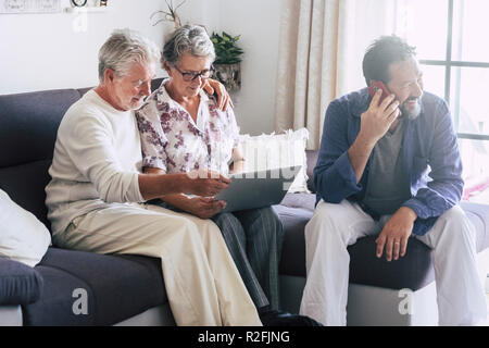 adult senior and middle age people at home. family daily real people scene with sofa and laptop. couple using internet and man speaking at the phone sitting on the sofa at home. indoor leisure activity for nice persons Stock Photo