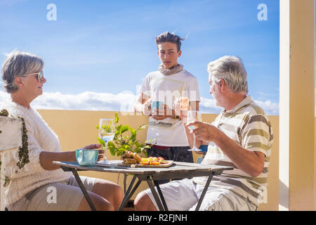grandfathers adult mature and teenager grandson enjoy outdoor in the terrace some leisure with food and drinks. ocean and city view, vacation sunny day nice weather concept and background. happy people family together Stock Photo