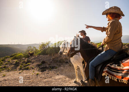 couple in vacation in tenerife ride horses in the nature. wind mill on the background and sunny colored day. dog and animals outdoor leisure activity for great therapy and friendship Stock Photo