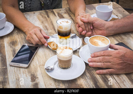 People drinking coffee and cappuccino at the bar over a wooden table with drinks and mobile phone technology. Socializing and love conept for adult man and woman waiting other friends Stock Photo