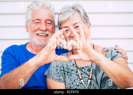playful beautiful cheerful caucasian adult senior couple enjoying lifestyle toghetner with smile and laugh doing heart with hands. love and partnership forever concept for happy man and woman people Stock Photo