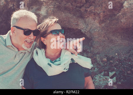 together forever for aged man and woman caucasian stay together under the sunlight looking the place around. rocks background for vacation concept Stock Photo